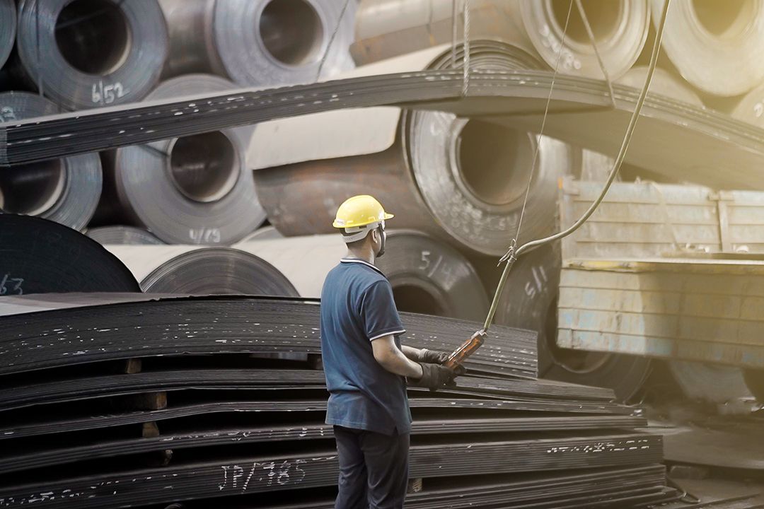 Worker guiding a crane hook over stacked steel plates in the Dmsons warehouse